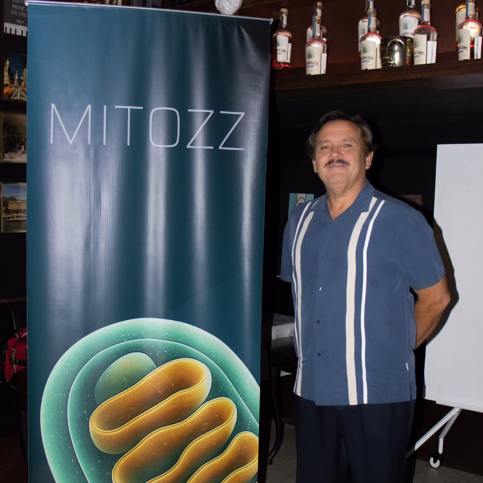 CMO and co-founder Francisco Villarreal standing next to a vertical Mitozz banner featuring a mitochondria graphic during an event at Talento restaurant.