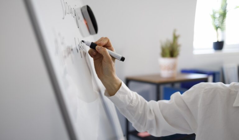 Person writing concepts on a whiteboard while analyzing complex systems.