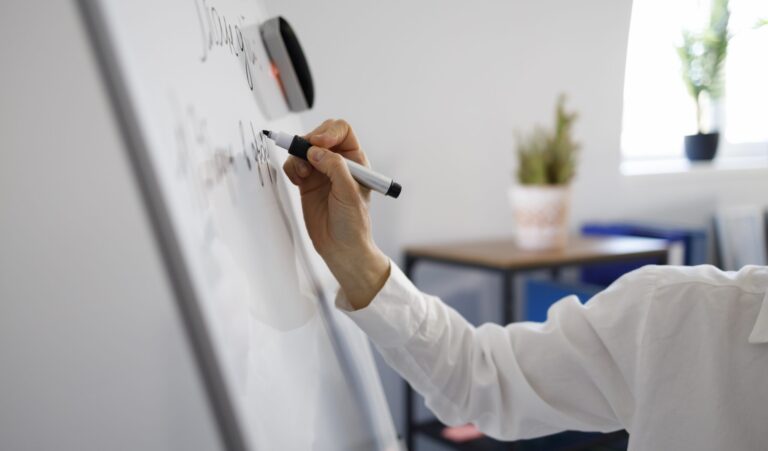 Person writing concepts on a whiteboard while analyzing complex systems.