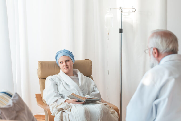 Person receiving cancer treatment seated in a clinic, speaking with a healthcare professional during recovery with low mitochondrial health. Mitozz