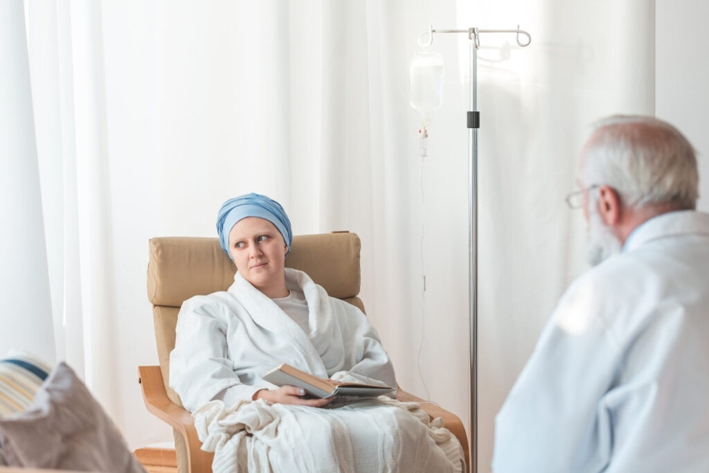 Person receiving cancer treatment seated in a clinic, speaking with a healthcare professional during recovery with low mitochondrial health. Mitozz