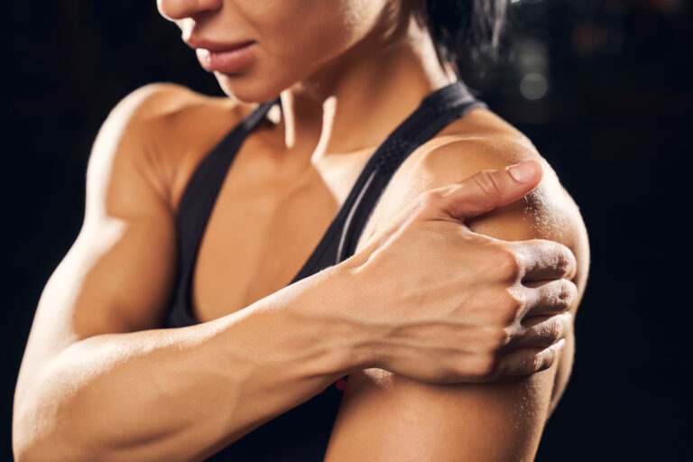 Muscular woman in gym attire holding her shoulder, close-up on arm and shoulder suggesting sore muscle. Mitozz, (-)-epicatechin