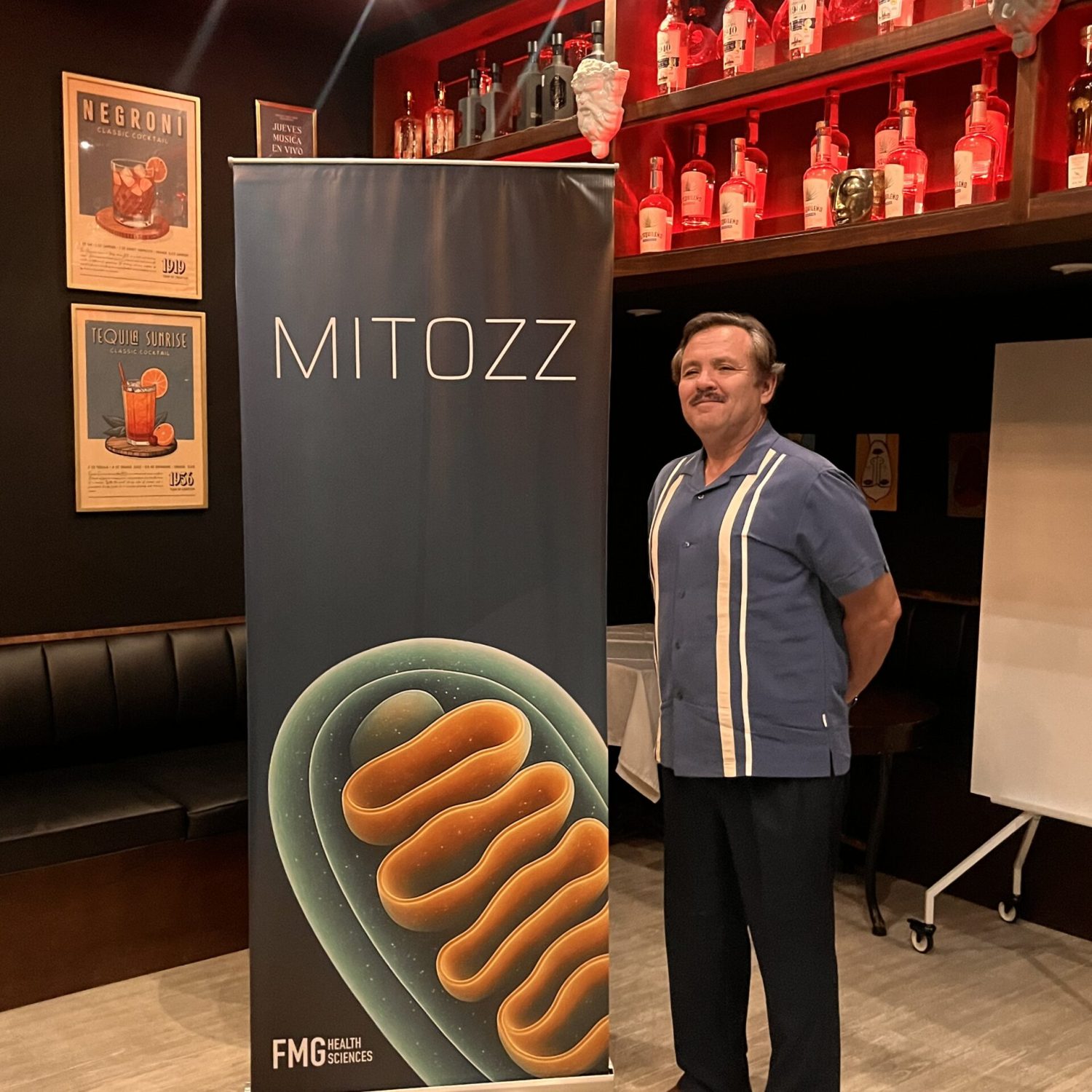 Speaker at Mitozz Events standing beside the official mitochondrial health banner during a wellness presentation.