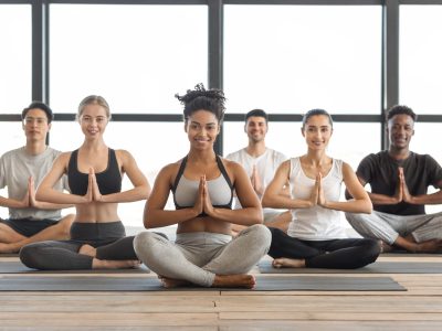 Wellness Concept. Happy Multicultural Young People Practicing Yoga In Modern Light Studio, Sitting In Lotus Position, Smiling At Camera, Copy Space